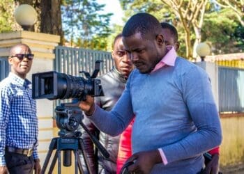 African cameraman looking into camera as two men look on